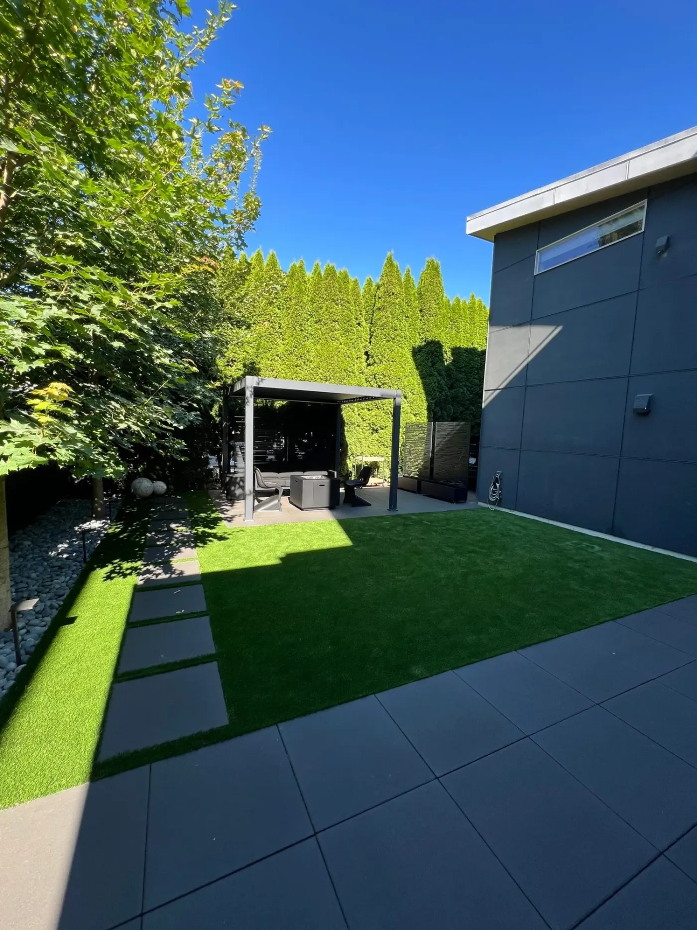 The same garden from the house: large concrete paver planks set into the turf lawn leading to the pergola