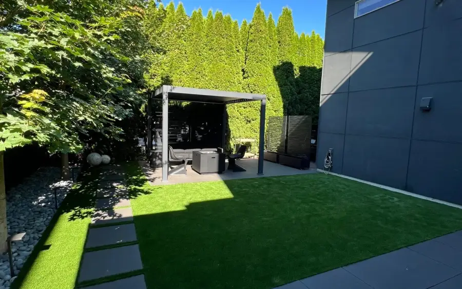 Large concrete paver planks set into an artificial turf lawn beside a dark modern house