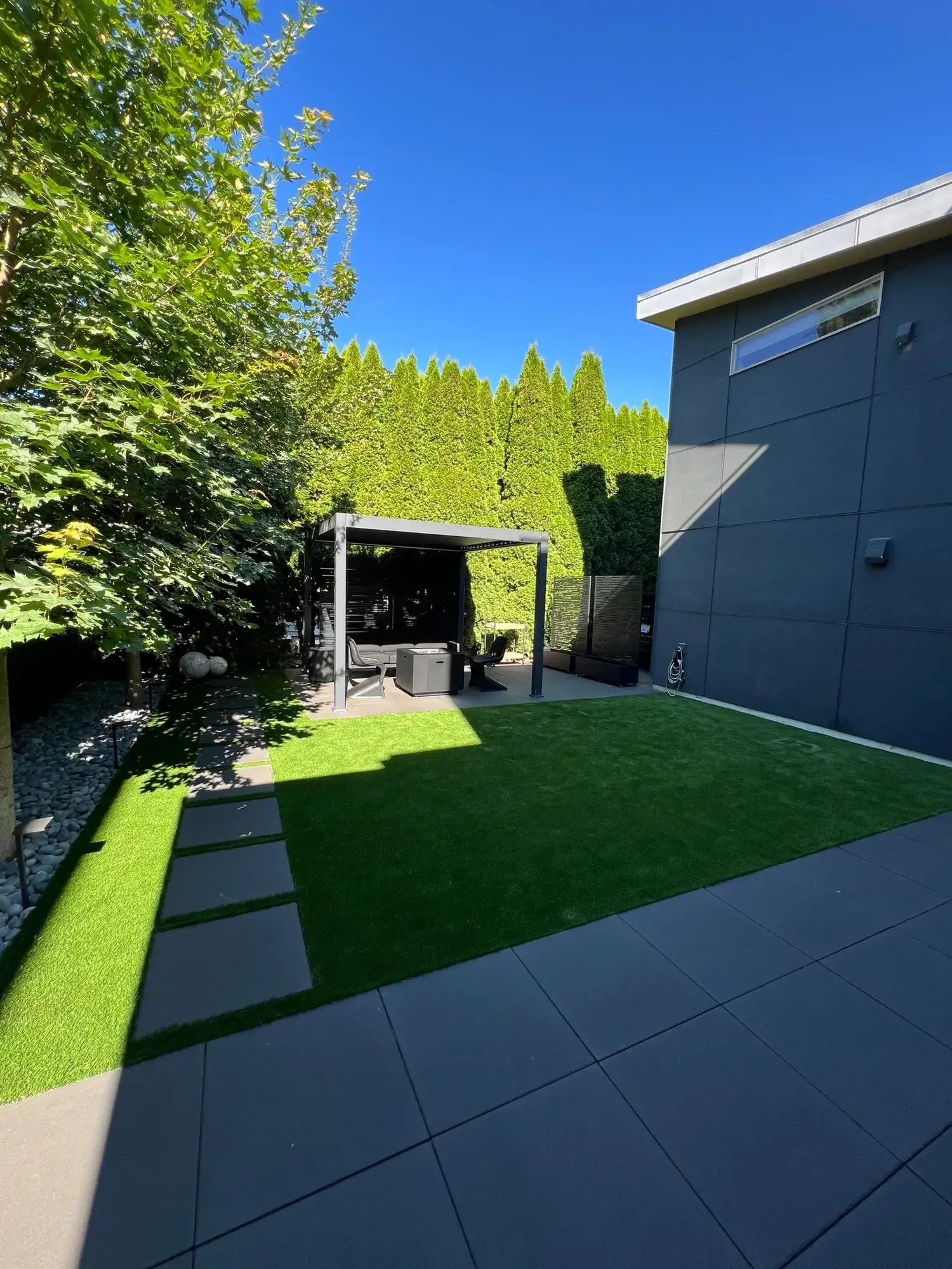 Large concrete paver planks set into an artificial turf lawn beside a dark modern house