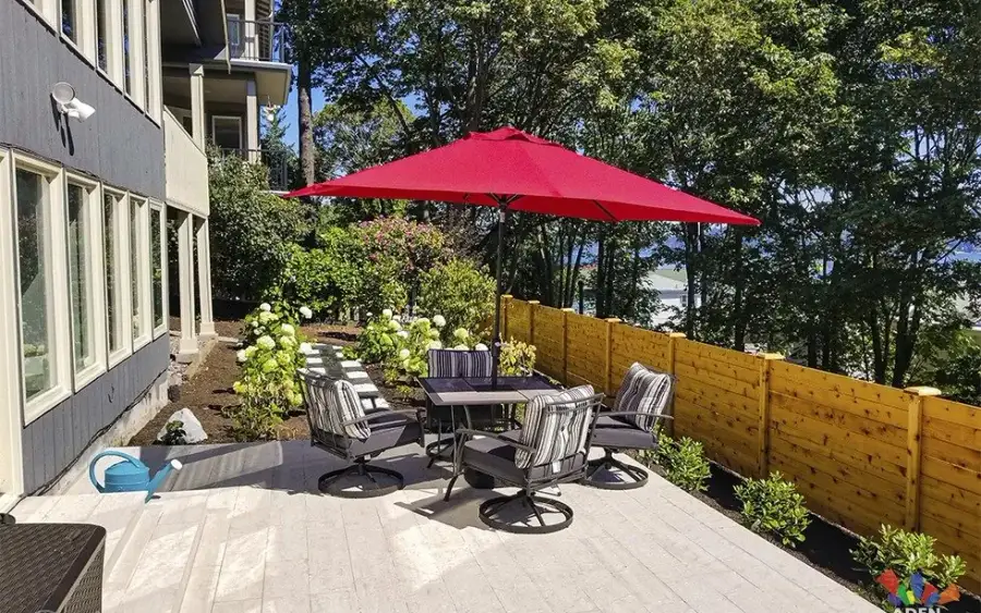 Large-format paver terrace with outdoor dining furniture beside a multi-unit building and cedar fence