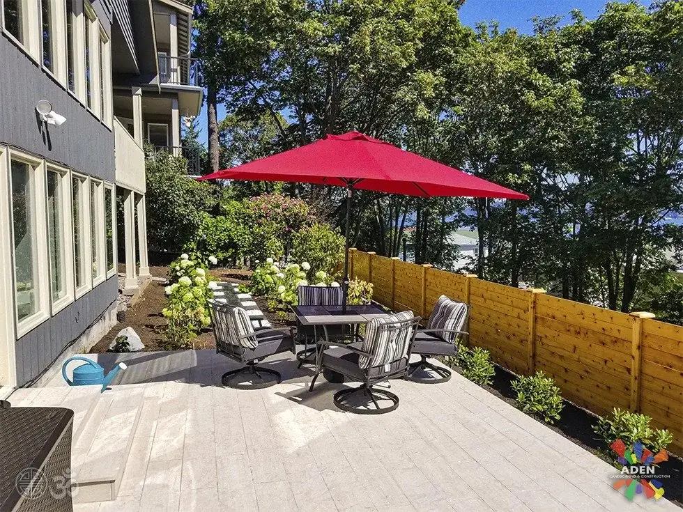 Large-format paver terrace with outdoor dining furniture beside a multi-unit building and cedar fence