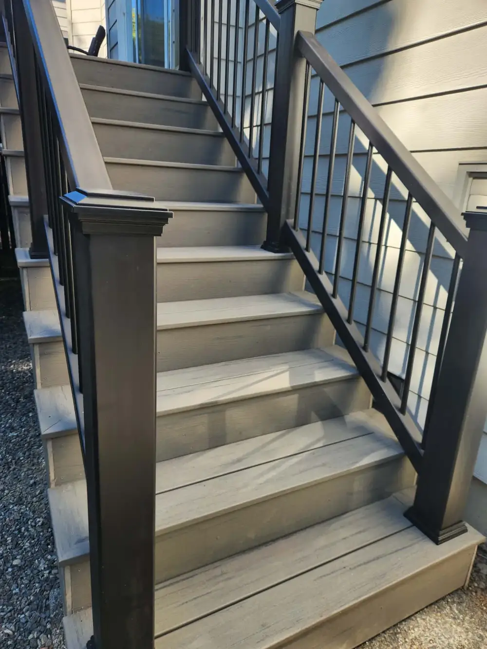 New composite deck stairs with a black aluminium railing rising and turning to a side door on a grey-sided Bothell house