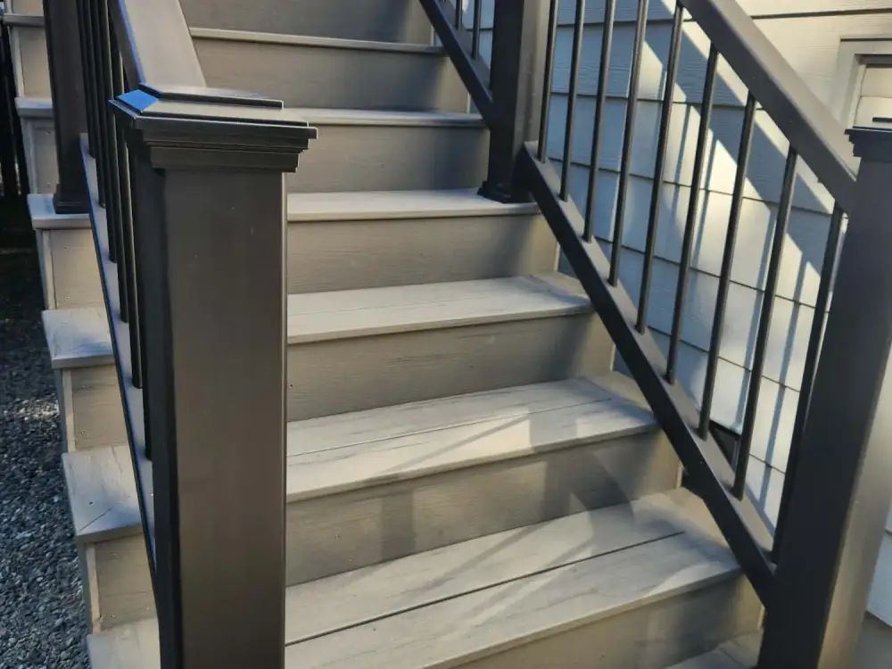 New composite deck stairs with a black aluminium railing rising and turning to a side door on a grey-sided Bothell house