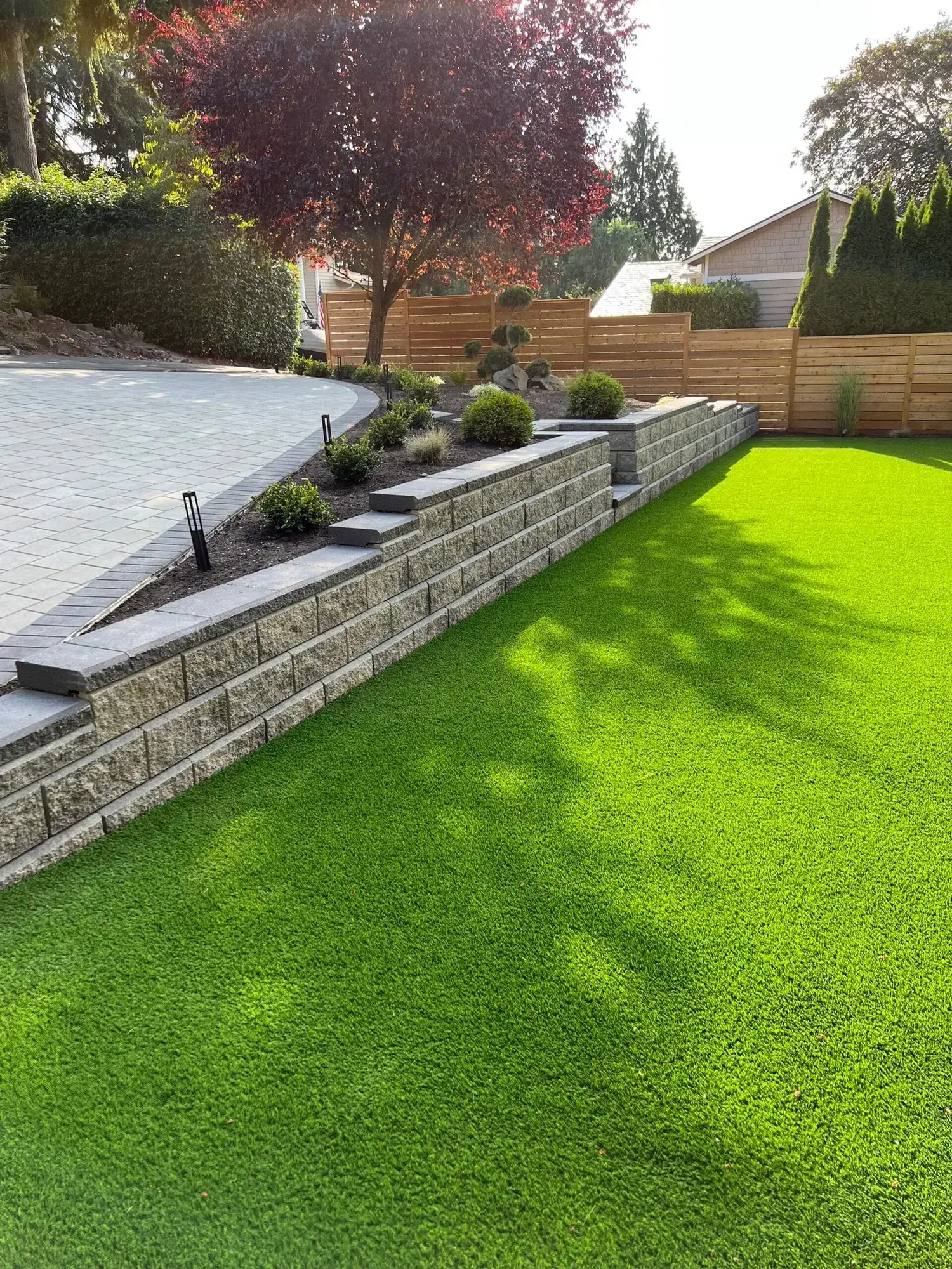 Block retaining wall holding a level artificial turf lawn against a cedar fence