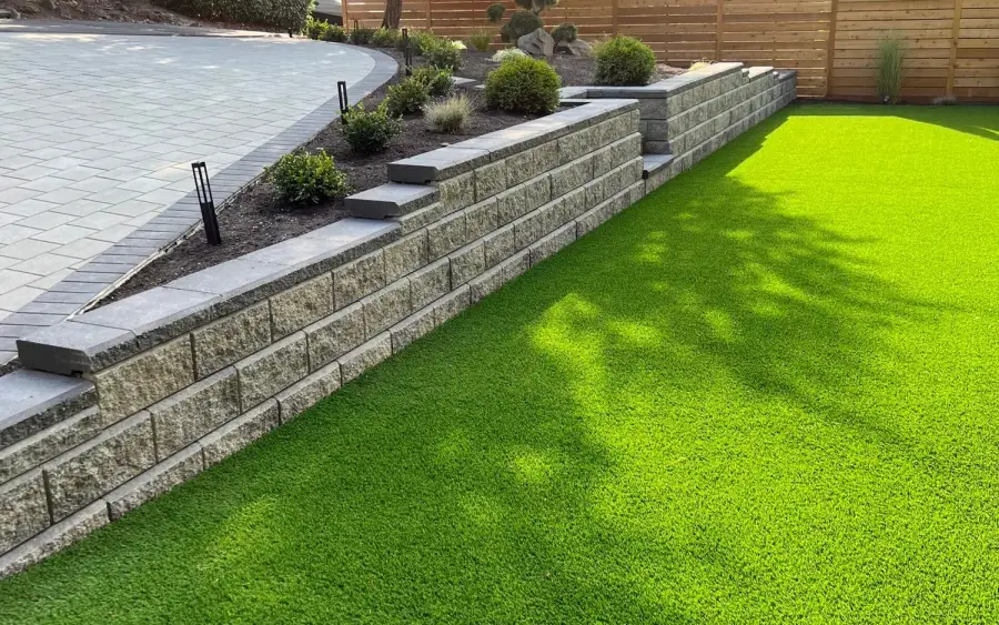 Block retaining wall holding a level artificial turf lawn against a cedar fence in Bothell