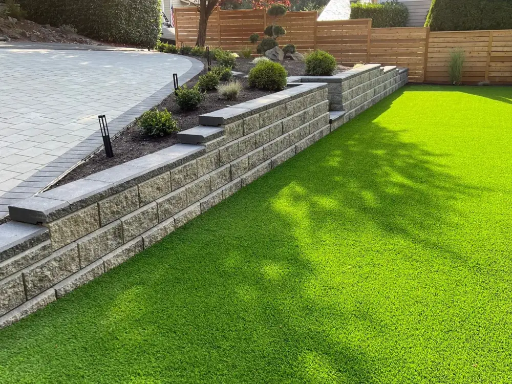 Block retaining wall holding a level artificial turf lawn against a cedar fence