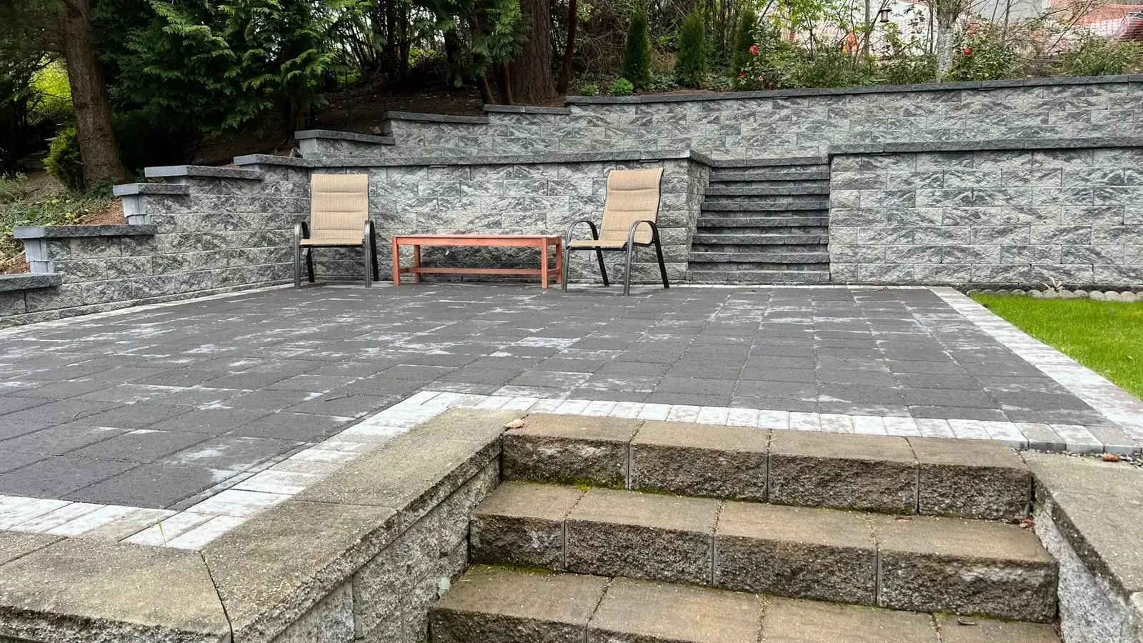 Terraced grey stone patio with wide steps and a seating area on a steep back garden