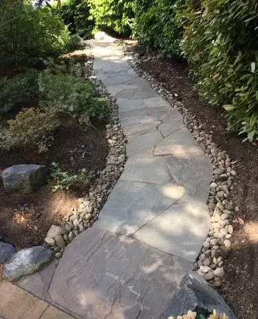 Flagstone stepping path curving through shade planting with a river rock edge running down both sides