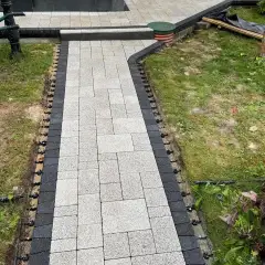 Light grey paver walkway with a charcoal border course under installation, edge restraint pinned along both sides