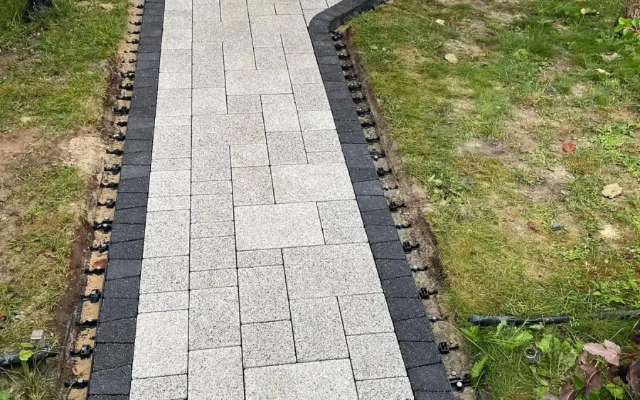 Light grey paver walkway with a charcoal border course under installation, edge restraint pinned along both sides