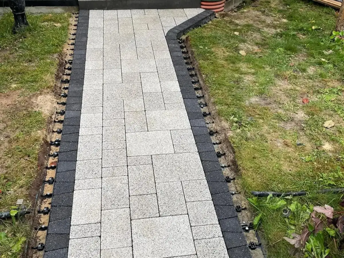 Light grey paver walkway with a charcoal border course under installation, edge restraint pinned along both sides