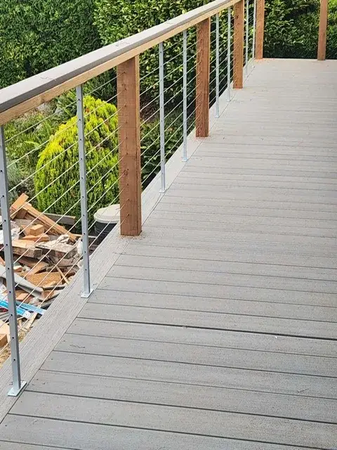 Composite deck walkway with cedar posts and stainless cable railing running beside a clipped hedge on a Kirkland property
