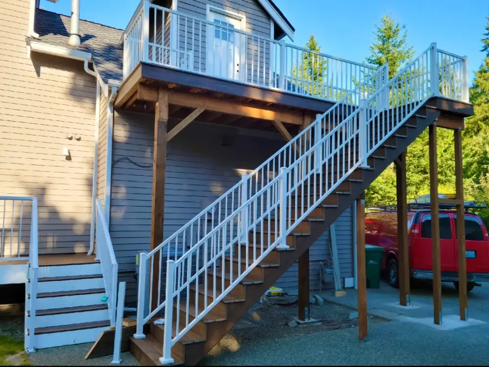 Elevated timber deck at first-floor level with white railings and a long staircase running down to a driveway
