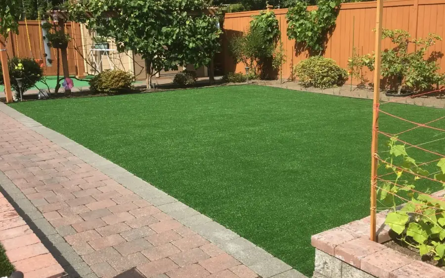 Rectangular artificial turf lawn edged with a grey border course beside a brick paver patio and cedar fence