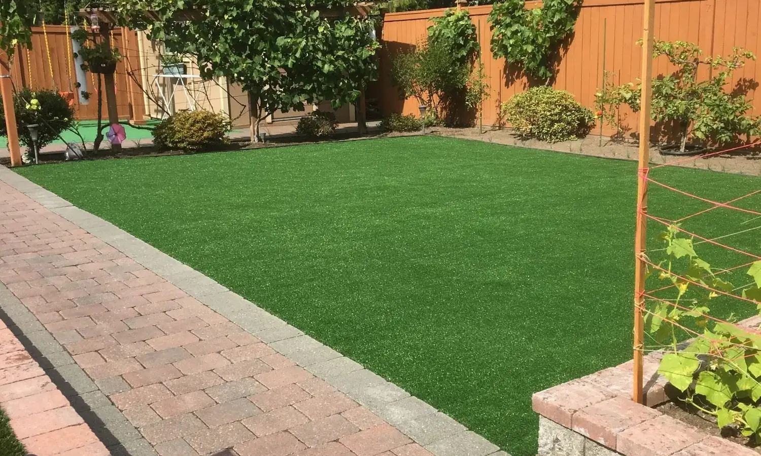 Rectangular artificial turf lawn edged with a grey border course beside a brick paver patio