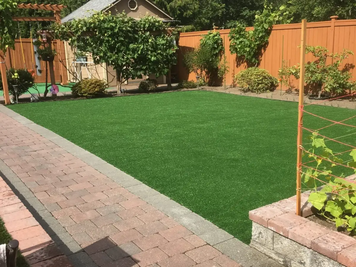 Rectangular artificial turf lawn edged with a grey border course beside a brick paver patio and cedar fence
