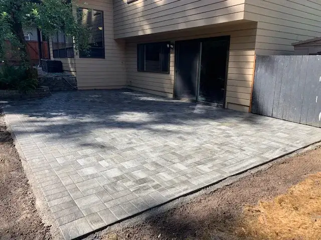 Large grey paver patio in a random pattern laid up to a sliding door, with the compacted base still exposed around the edges