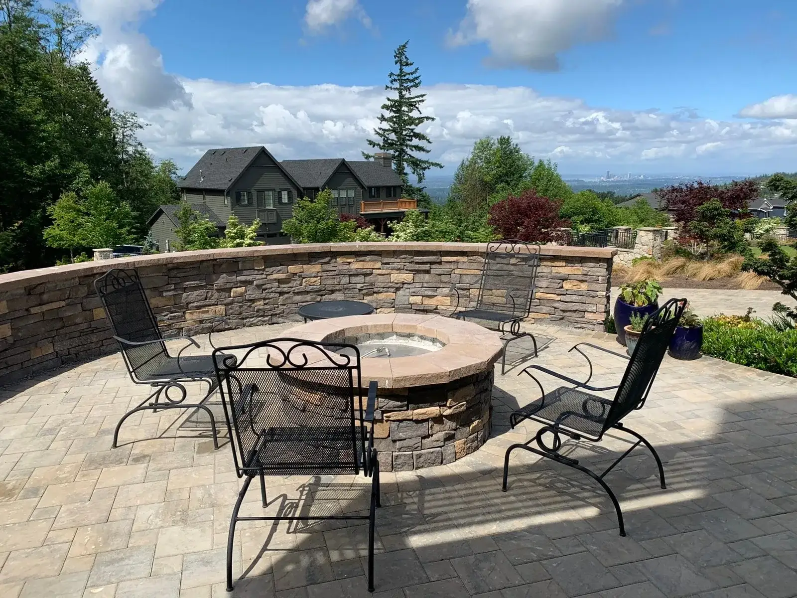 Circular stone fire pit and curved seat wall on a paver patio overlooking a valley view