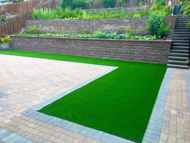 Long brick-faced retaining wall carrying raised vegetable beds above an artificial turf lawn and paver terrace