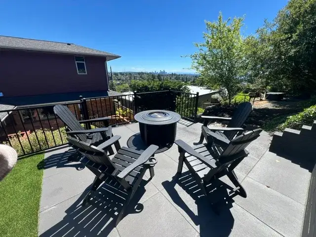 Grey slab terrace with a round fire table and black Adirondack chairs on a Magnolia hilltop, the Seattle skyline visible in the distance