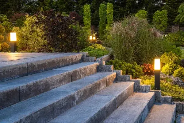 Wide stone steps lit at dusk by bollard lights, with ornamental grasses and clipped conifers on either side