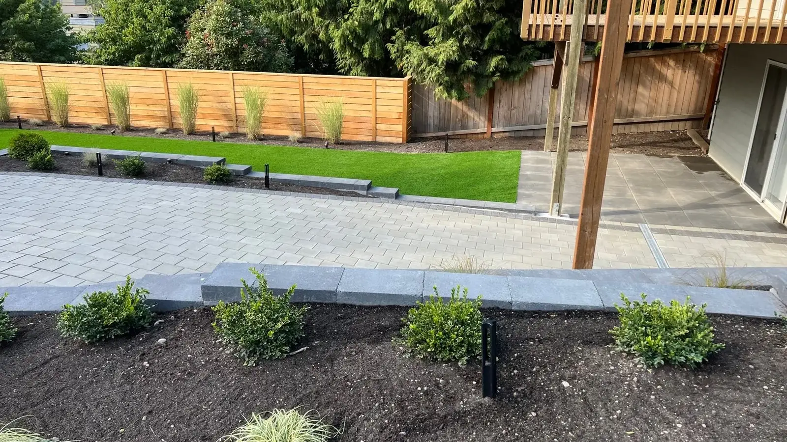 Grey paver patio with charcoal edging walls, turf lawn and freshly planted boxwood beds