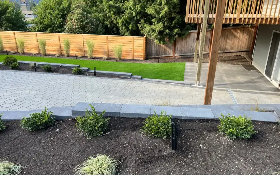 Newly completed landscape with a grey paver patio, charcoal edging walls, turf lawn and freshly planted boxwood beds