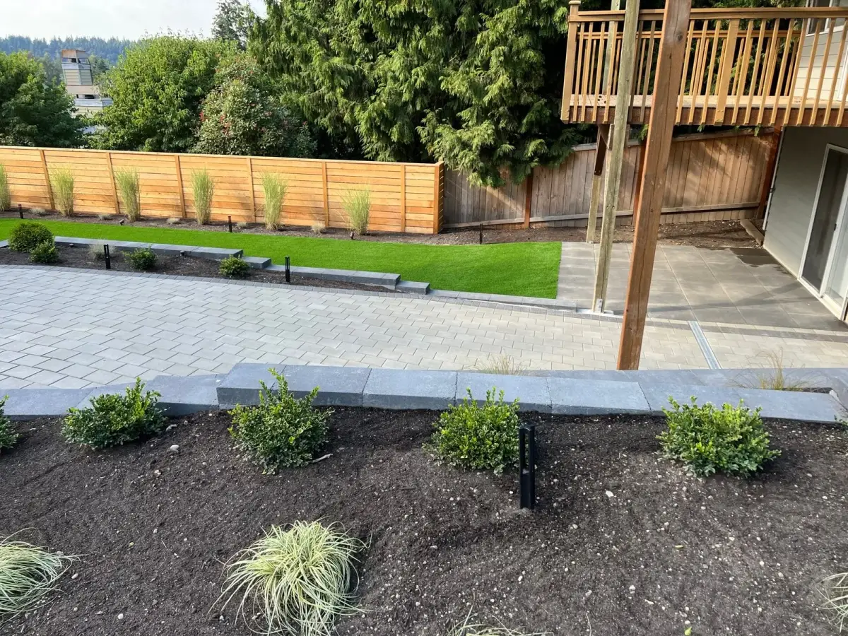 Newly completed landscape with a grey paver patio, charcoal edging walls, turf lawn and freshly planted boxwood beds