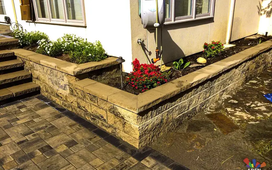 Stone-faced raised planting beds filled with fresh soil beside a paved path