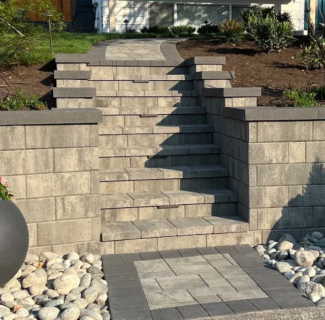 Block steps set between two retaining wall returns, with a paver landing at the bottom and river rock either side