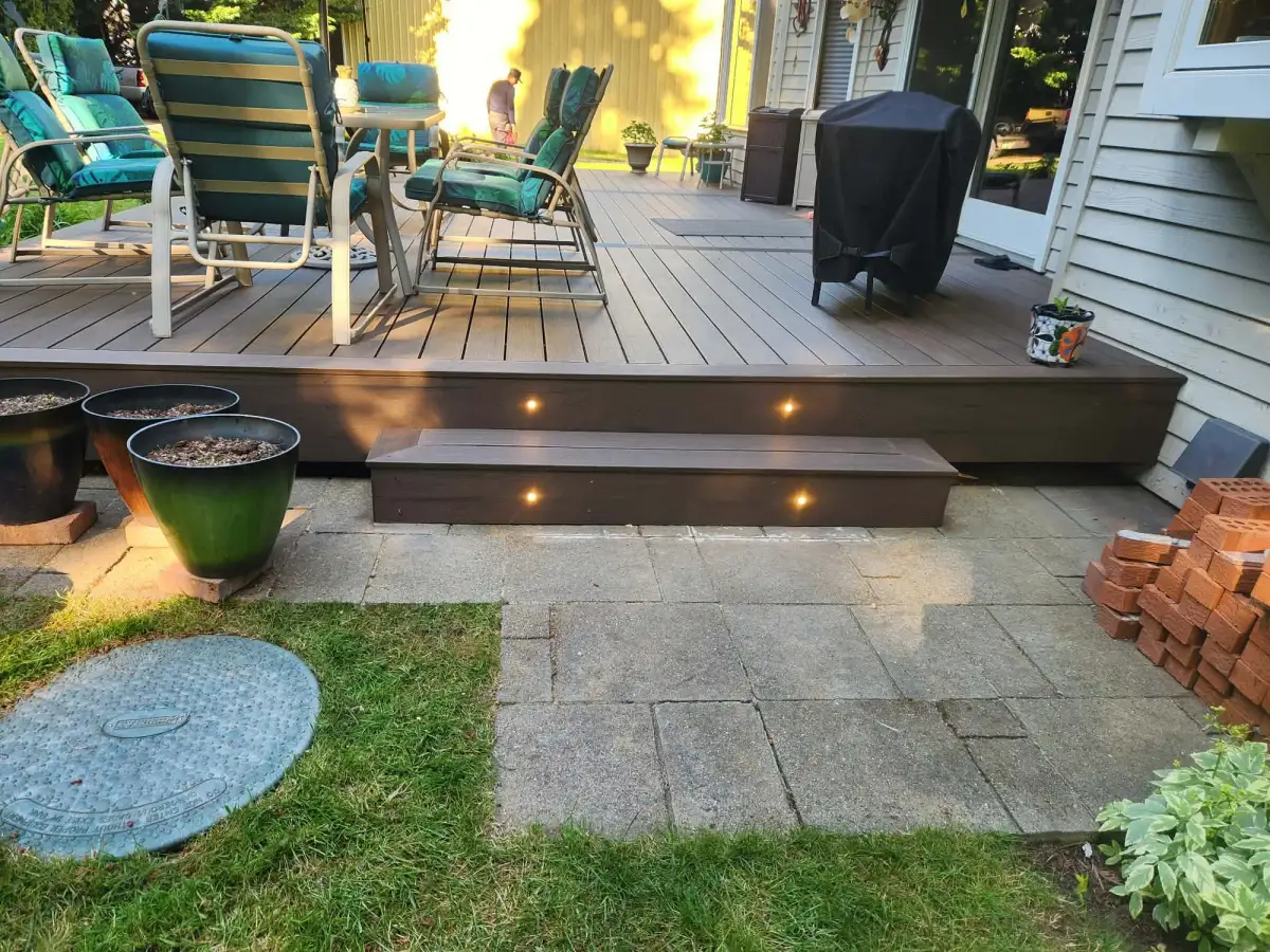 Composite deck with warm lights set into the step risers leading down to a paver patio at dusk in a Queen Anne back garden