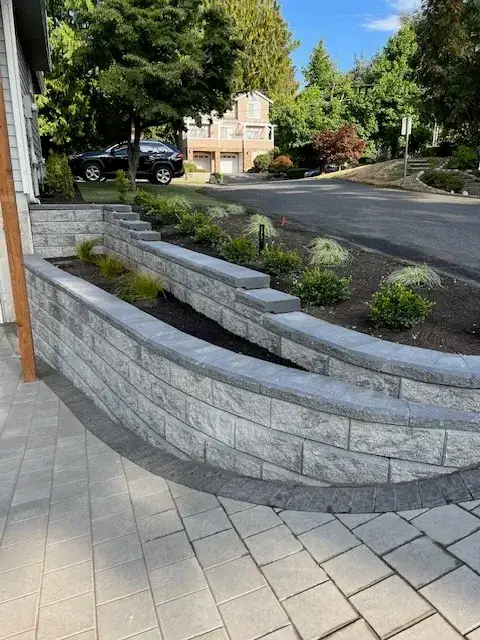 Curved grey block retaining wall with a capped top running along a front garden, with new planting behind and a paver walk in front