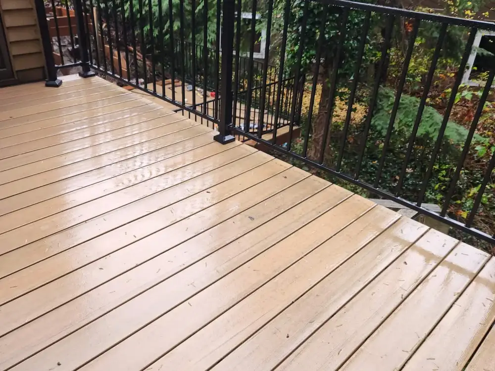 Rain-wet composite deck with black metal railing looking out into conifers and autumn foliage at a Redmond house