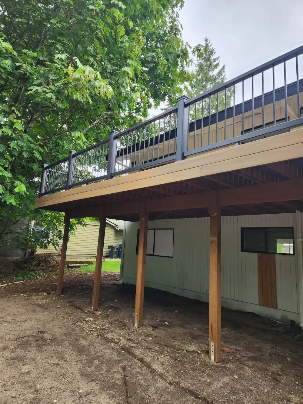 Elevated composite deck on cedar posts with black aluminium railing spanning the back of a Redmond house above a daylight basement