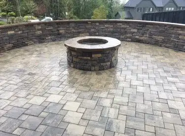 Round stone fire pit set into a paver patio inside a curved seat wall of stacked stone