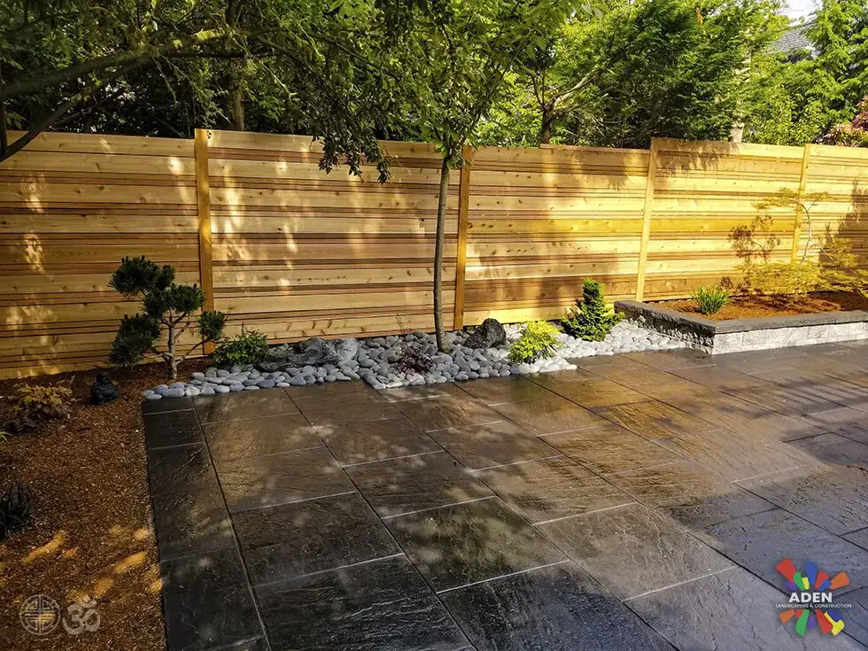 Wet large-format grey slab terrace with a horizontal cedar slat screen behind it and a white rock border