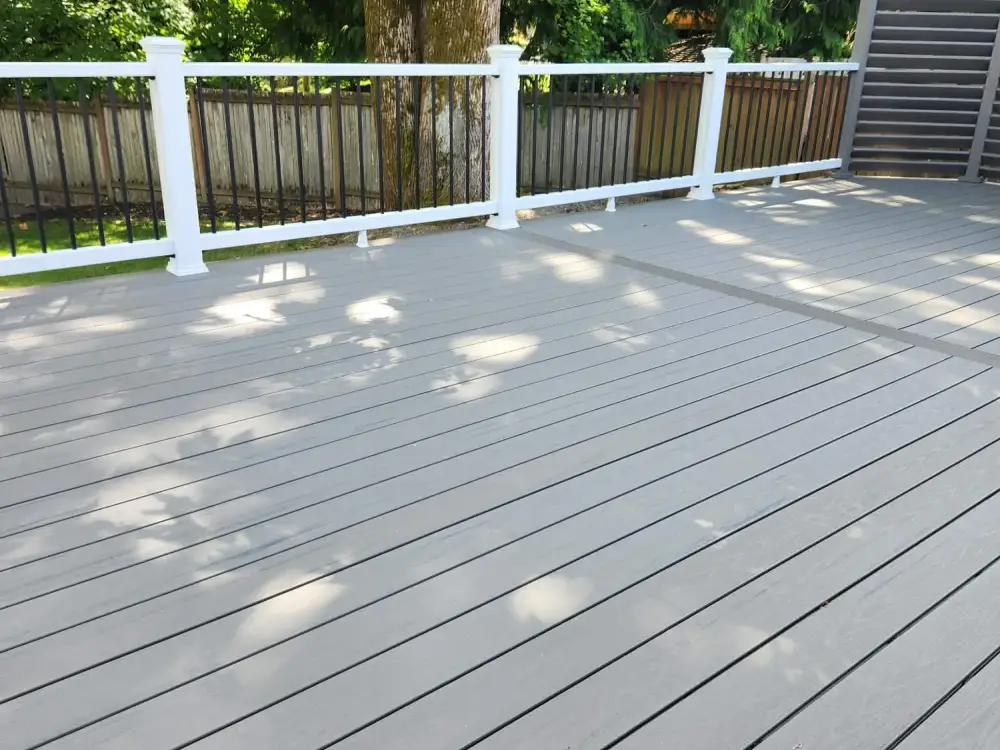 Large grey composite deck with white posts and black metal balusters beneath a mature maple in a fenced Sammamish garden