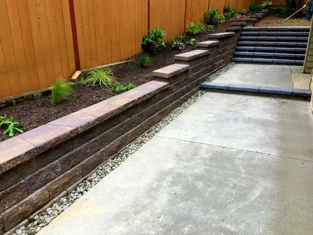 Two-tier block retaining wall with stone steps and new planting on a sloped side yard