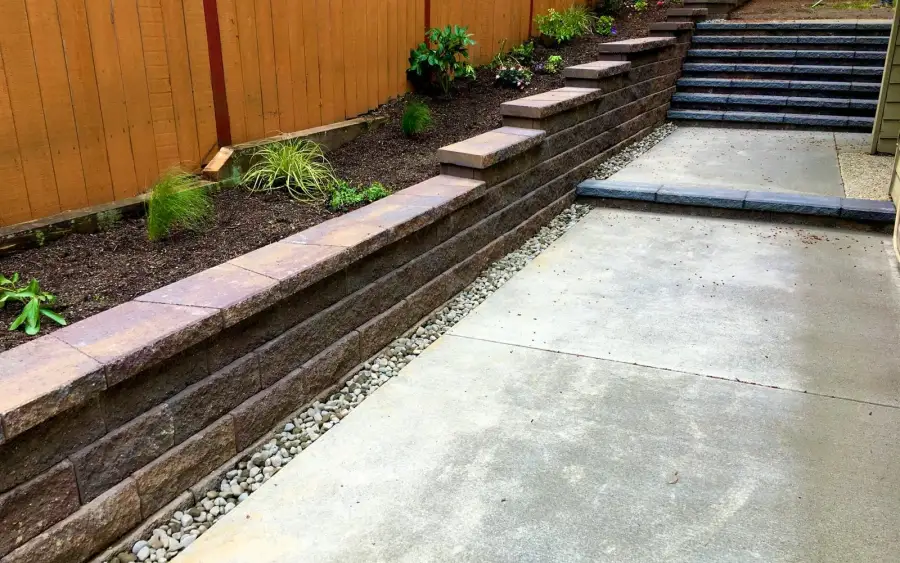 Two-tier block retaining wall with stone steps and new planting on a sloped side yard