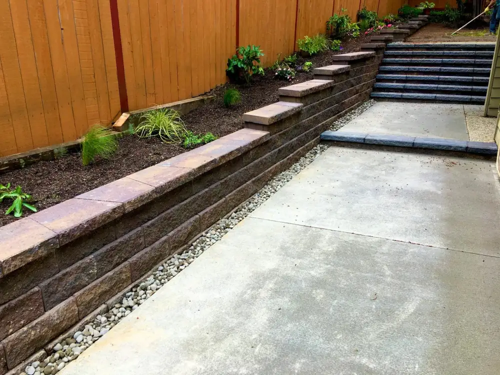 Two-tier block retaining wall with stone steps and new planting on a sloped side yard