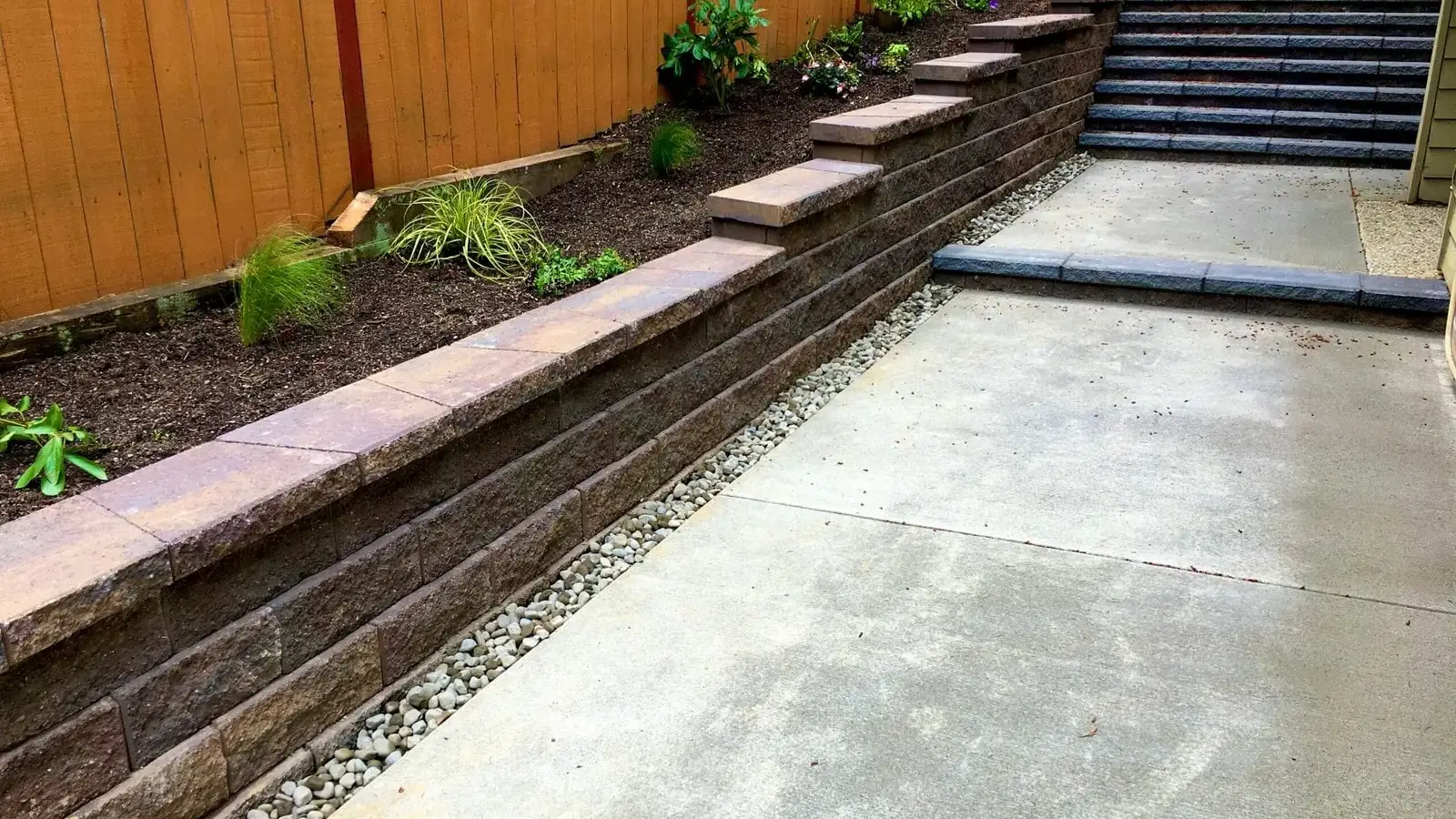 Two-tier block retaining wall with stone steps and new planting on a sloped side yard