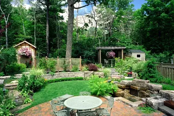 Brick paver terrace with a garden table below a stone rockery and waterfall, with a timber pergola and lattice screens on the level above