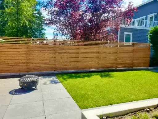 Horizontal cedar slat screen fence along a small city garden with a concrete patio, a mesh fire bowl and an artificial turf lawn