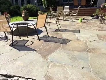 Irregular flagstone patio with a round fire bowl and mesh chairs, laid tight against the back of the house