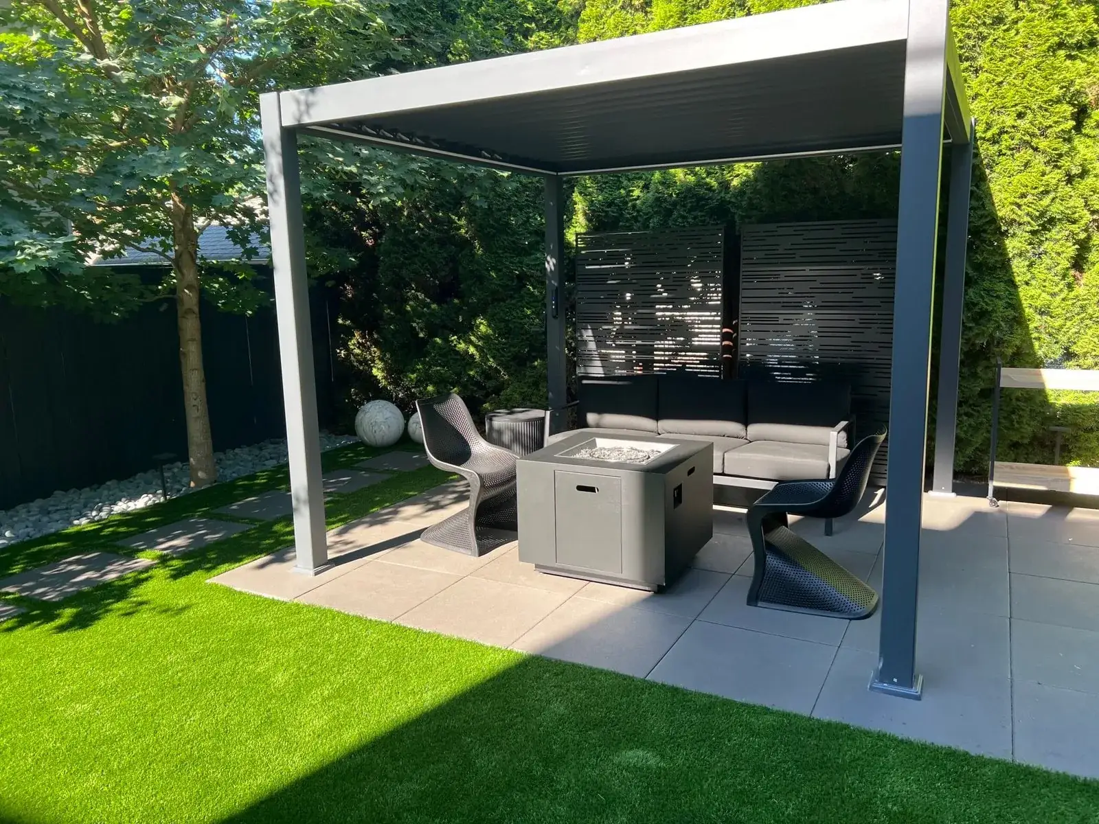 Covered outdoor lounge with a fire table beside an artificial turf lawn, built by Aden Landscaping
