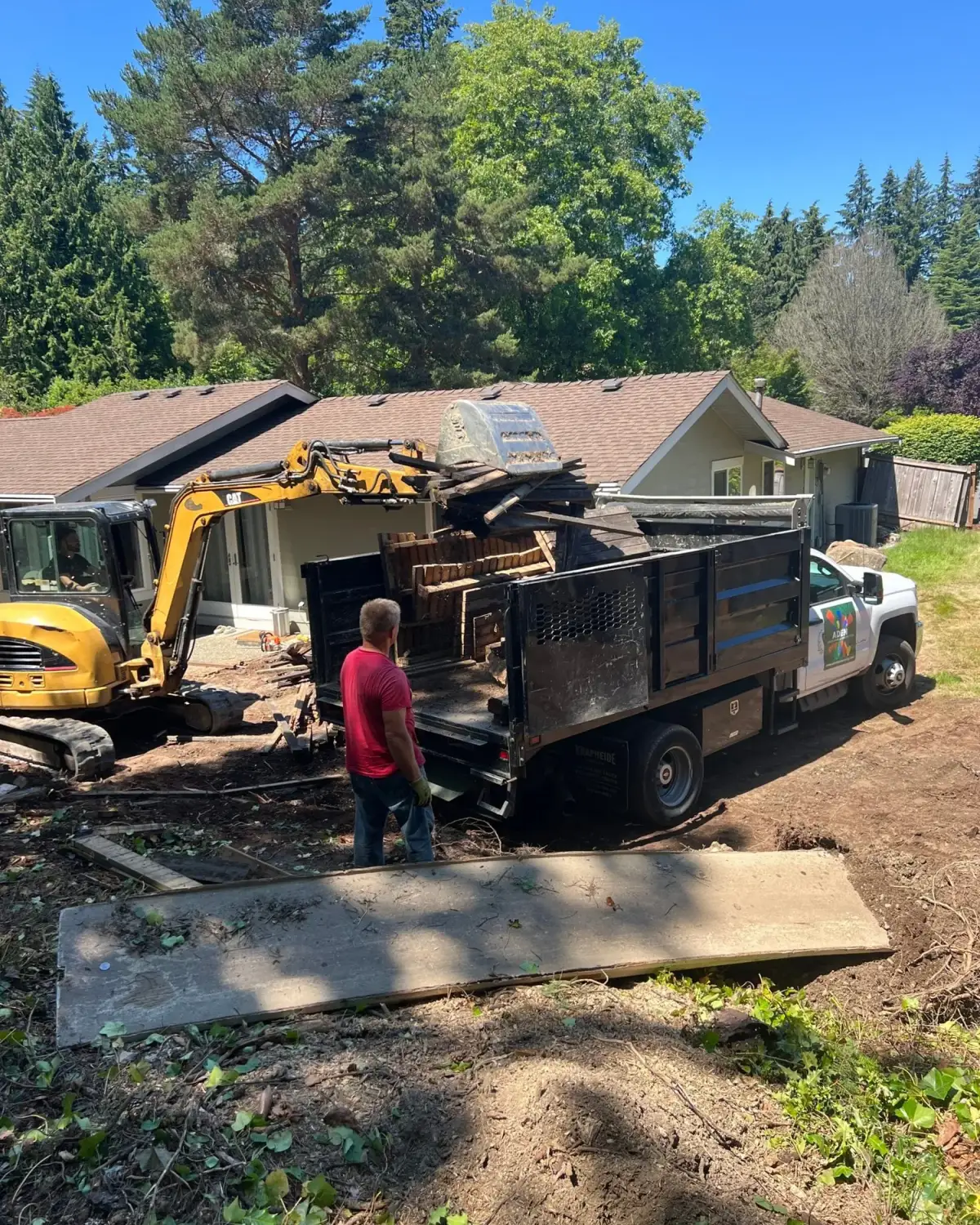 Excavator loading cleared timber and vegetation into an Aden Landscaping dump truck