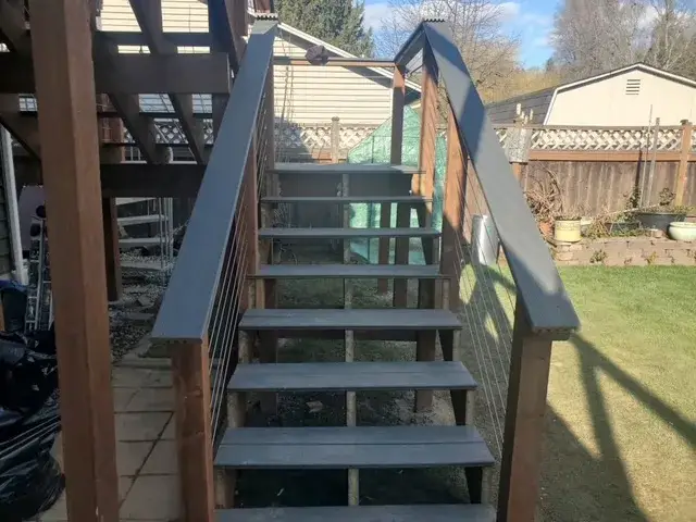 Composite deck stairs with cedar posts and stainless cable railing running down from a raised deck to a lawn at a Shoreline house