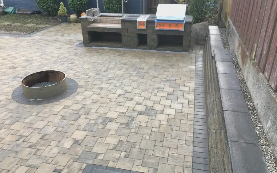 Built-in outdoor kitchen island and fire pit on a paver patio with a low seat wall in Shoreline