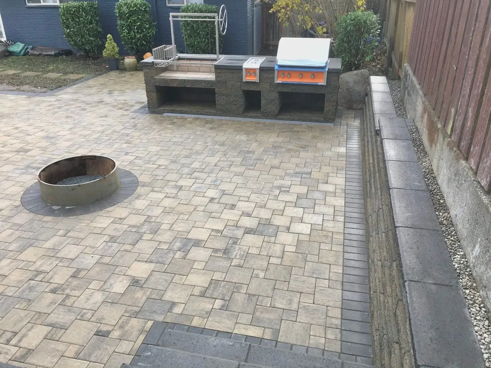 Built-in outdoor kitchen island and fire pit on a paver patio with a low seat wall