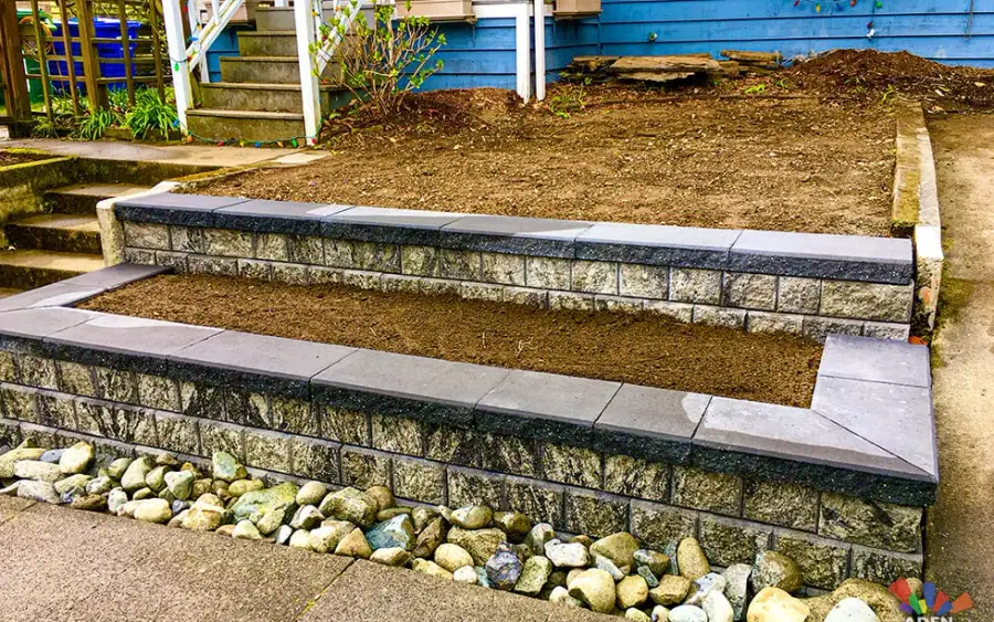 Capped two-tier block retaining walls with a cobble drainage bed and steps on a Shoreline front garden